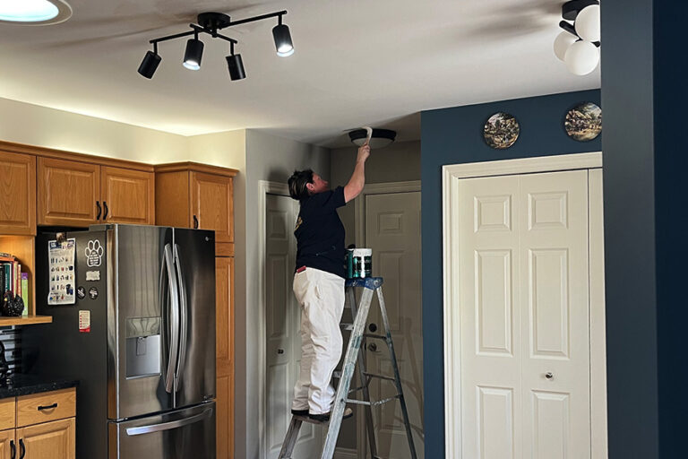 A woman painting a ceiling in a kitchen.