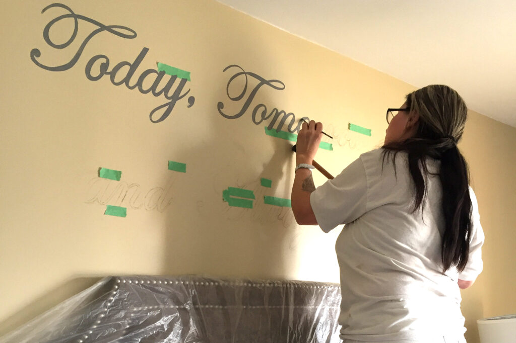 A woman painting a wall in a bedroom.