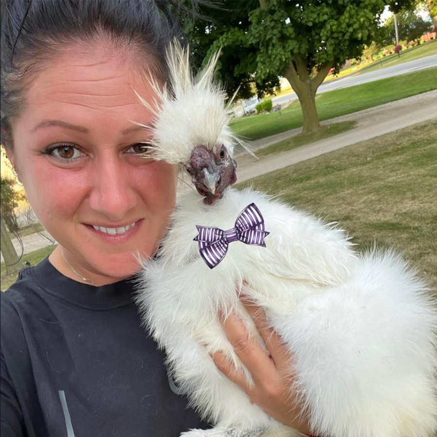 A woman holding a white rooster in a bow tie.